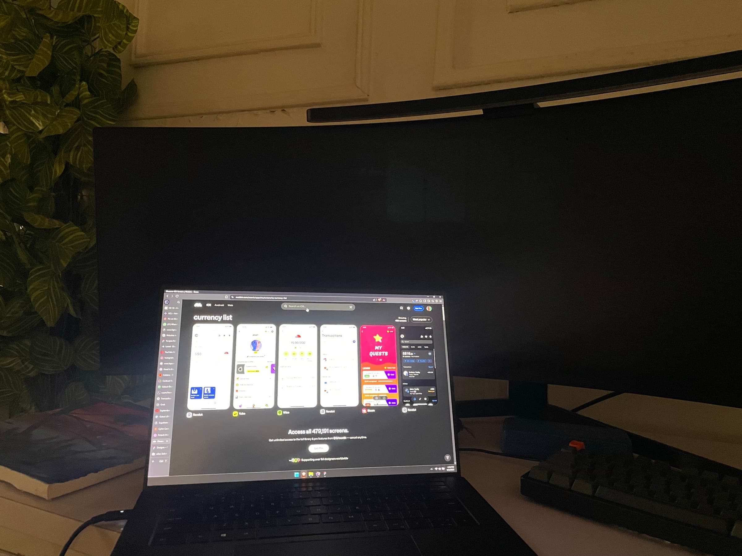 A laptop showing app screens on a desk at night, beside a plant and a keyboard